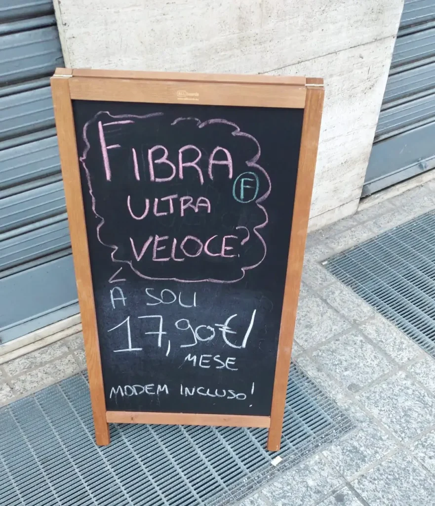 Cartello in strada con scritta "Fibra ultra veloce a 17,90€ al mese modem incluso", simbolo della guerra dei prezzi nella telefonia