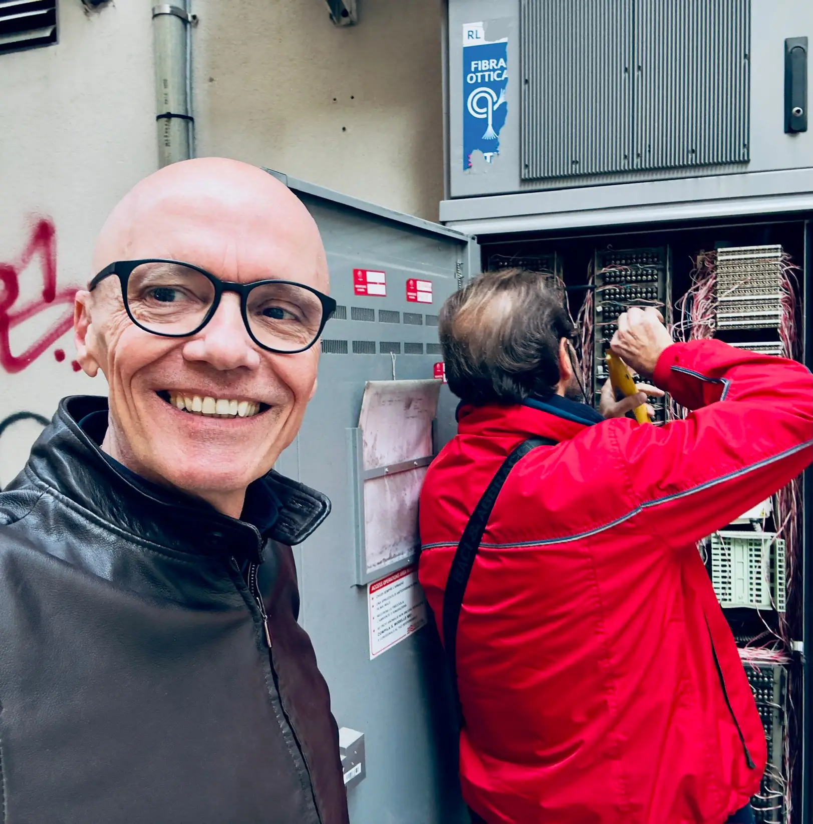 Massimo Marucci sorride accanto a un tecnico FiberCop che lavora a un armadio della rete in fibra ottica